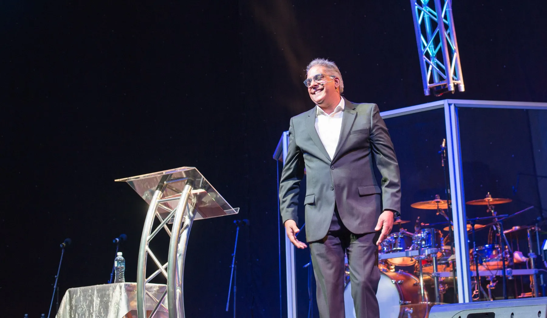 Dr RJ Sing in a grey suit, smiling on stage