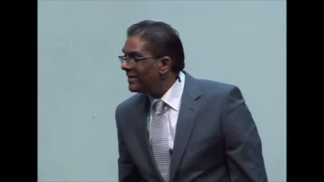 Dr RJ Sing smiling as he preaches in a grey suit, 2012