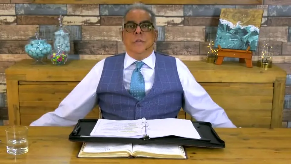 Dr RJ Sing teaching from his desk with an open Bible and notes
